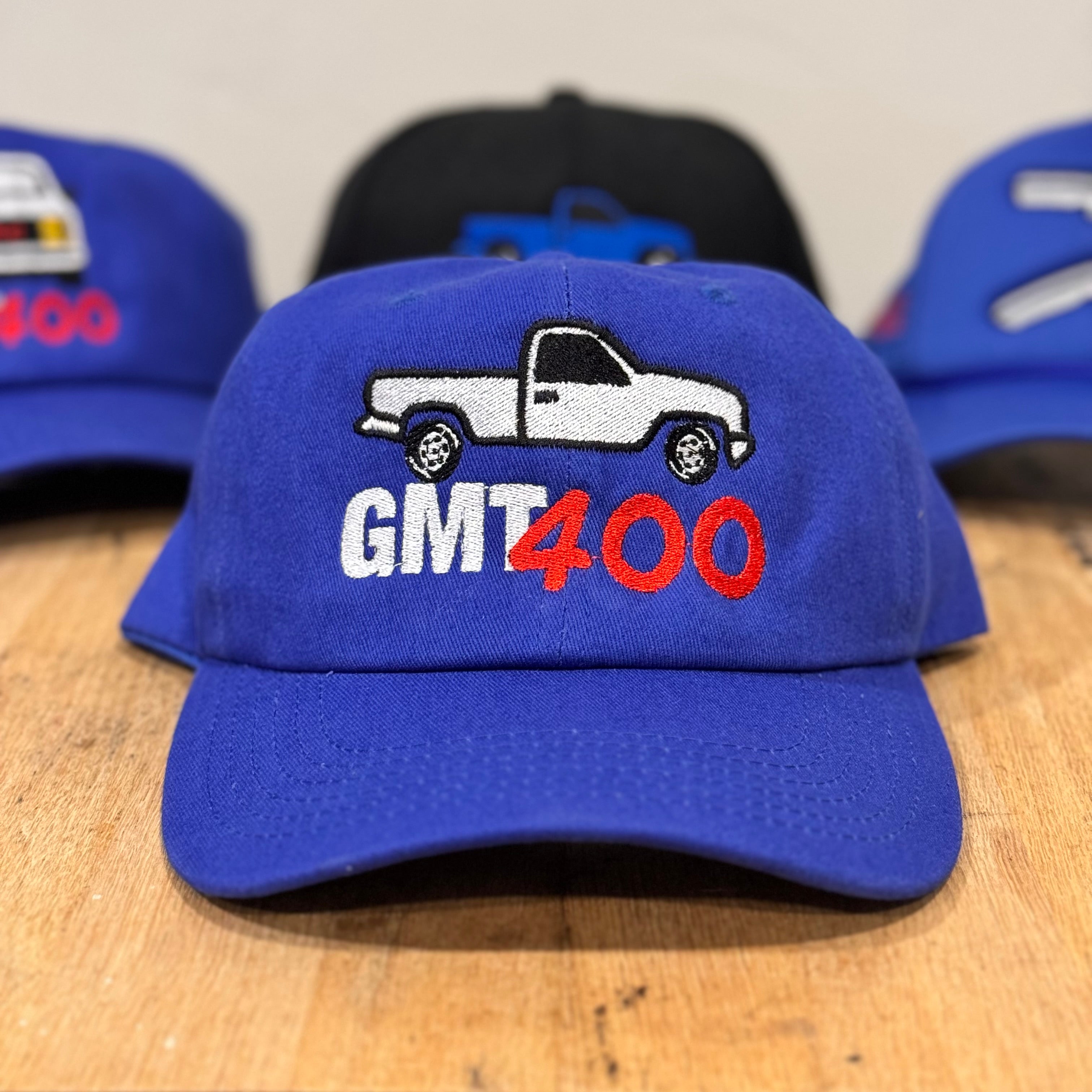 Blue cap with truck graphic and 'GMT400' text on a wooden surface